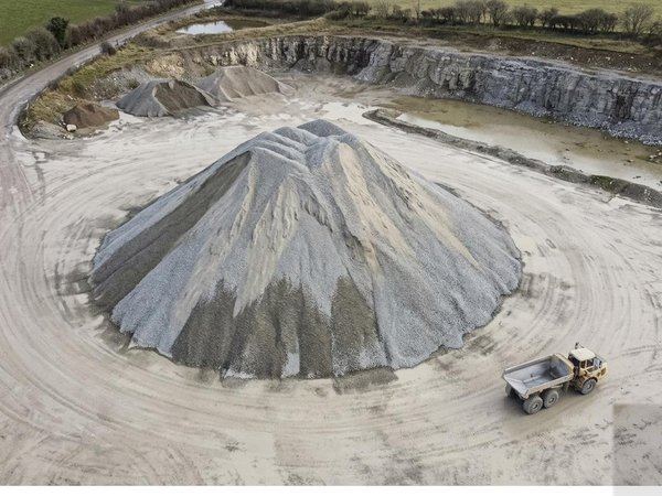 A drone photograph of a stone stockpile in a quarry with a dump truck beside it.